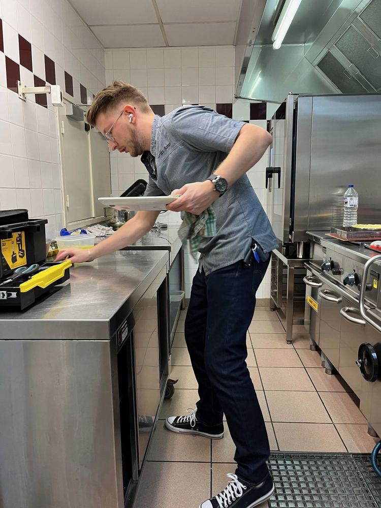 Charles Baras, en veste de chef pâtissier à son nom, dresse une assiette dans une cuisine de restaurant.