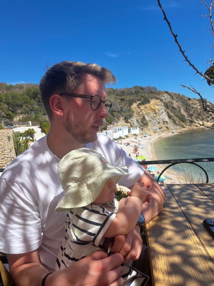 Charles porte sa fille face à une crique, en Espagne.