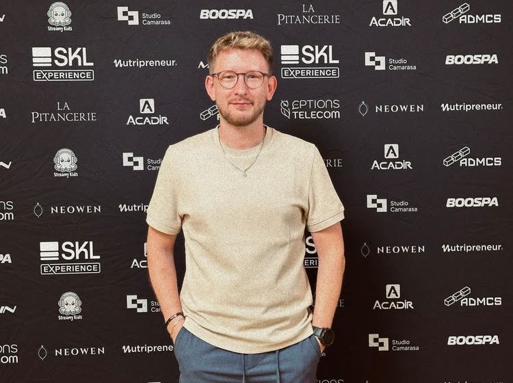Charles Baras devant le mur de partenaires de SKL Experience.